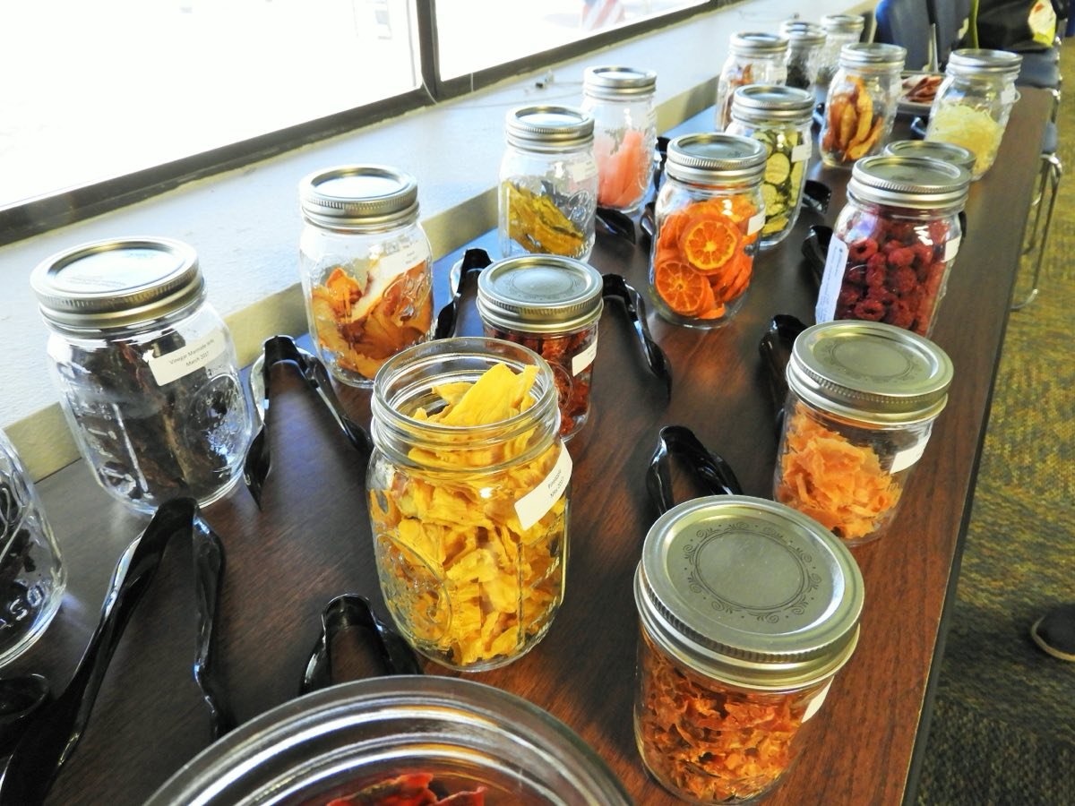 Glass jars of dried mango, orange slices, peppers and other preserved produce